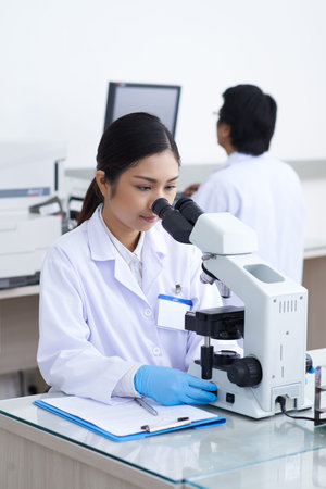 Pretty Vietnamese medical worker using modern microscope in clinic
