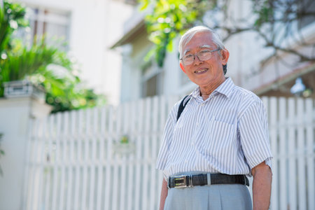 Aged Vietnamese man in glasses standing in front of his houseの写真素材