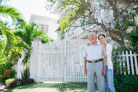 Senior Vietnamese man and his adult daughter standing in front of their houseの写真素材