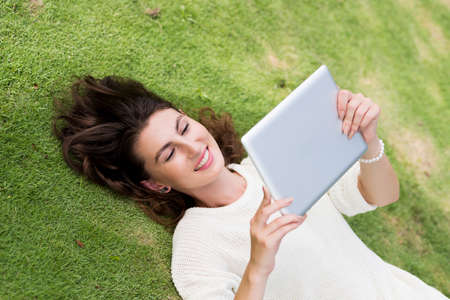 Smiling young woman with digital tablet lying on the grassの写真素材