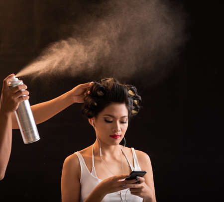 Hairdresser using hairspray to fix curls of beautiful Vietnamese womanの写真素材