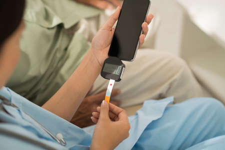 Hands with test strip and smartphone checking blood sugar level by glucose meter applicationの写真素材