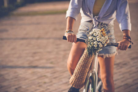 Cropped image of woman riding bicycle with wildflowers in basketの写真素材