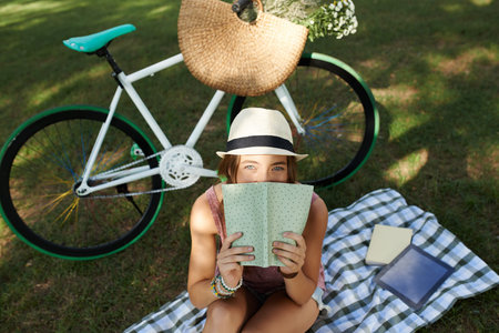 Lovely girl covering her lips with a book and looking at cameraの写真素材