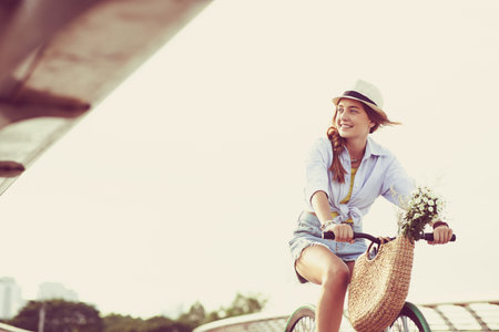 Happy lovely girl riding bicycle with flowers in basketの写真素材