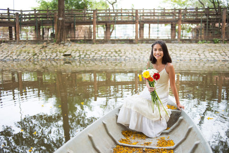 Pretty mixed-race woman sitting in boat with bouquet of flowersの写真素材