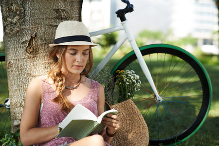 Pretty young woman leaning against the tree and readingの写真素材