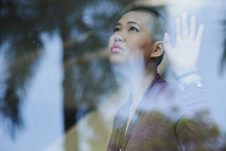 Bald beautiful woman looking through the window with hopeの写真素材