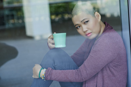 Portrait of sad Asian with a cup of tea sitting at windowの写真素材