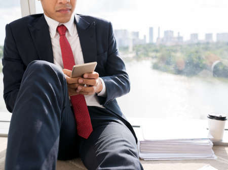 Cropped image of businessman sitting on the floor and text messagingの写真素材