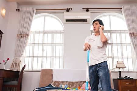 Househusband making phone call when cleaning the roomの写真素材