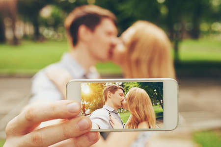 Man photographing himself kissing girlfriend, focus on the smartphone screenの写真素材