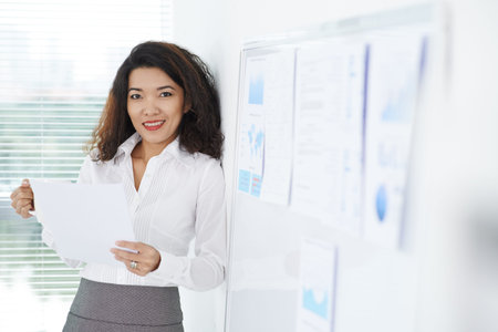 Portrait of smiling female manager with papers standing at the whiteboardの写真素材