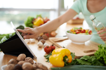 Woman checking recipe on digital tablet before seasoning saladの写真素材
