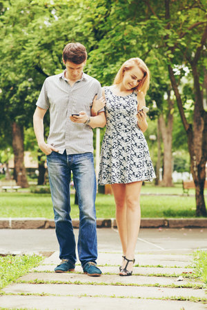 Young couple texting when walking in the parkの写真素材