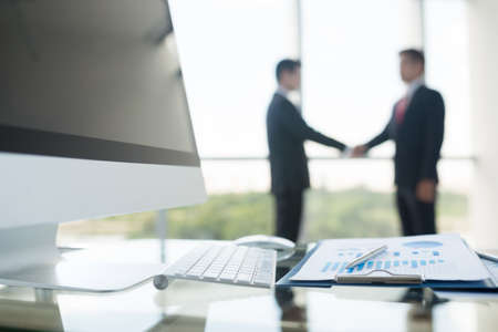 Table with financial document and business people shaking hands in backgroundの写真素材