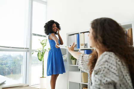 African-American business lady talking on the phone and giving document to her colleagueの写真素材