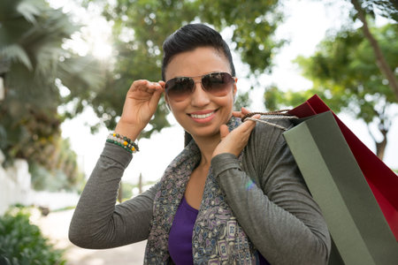Portrait of happy woman in sunglasses holding many shopping bagsの写真素材