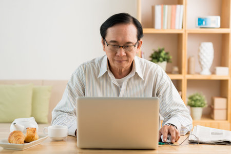 Senior Vietnamese man using laptop at home