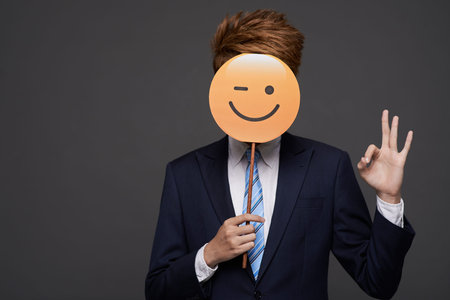 Businessman showing ok sign and covering head with winking faceの写真素材