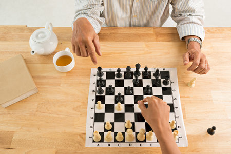 Hands of people playing chess at home view from above