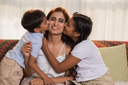 Indian brother and sister kissing their mother on both cheeksの写真素材
