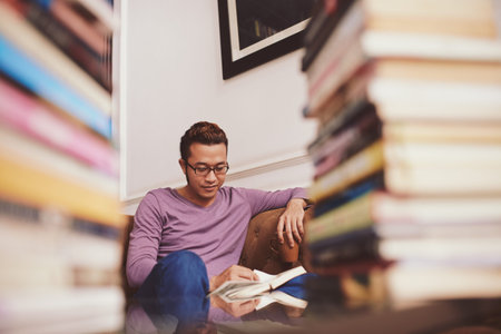 Smiling Asian man reading book and drinking tea in a library