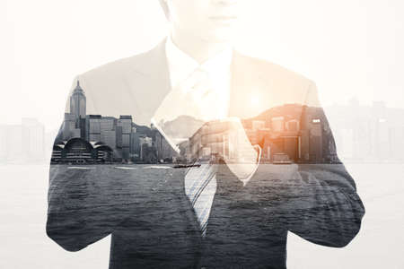 Double exposure of businessman adjusting tie and cityscapeの写真素材
