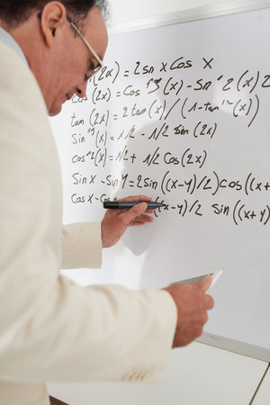 Mature teacher rewriting formulas in the digital tablet on the whiteboard