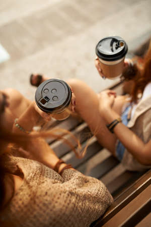 Female friends drinking fresh hot take-out coffee, view from the topの写真素材