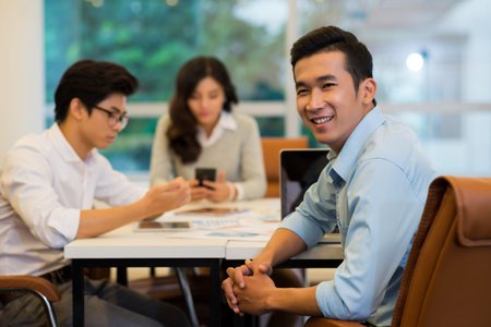 Portrait of cheerful Asian startup company founder having meeting with his colleaguesの写真素材