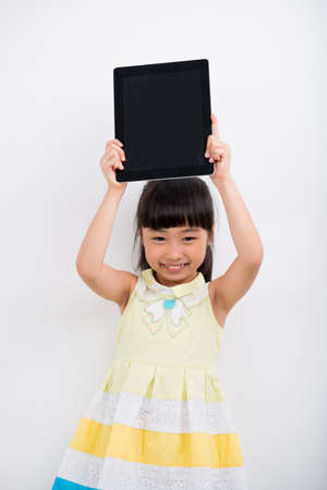 Portrait of little Asian girl holding digital tablet above her headの写真素材