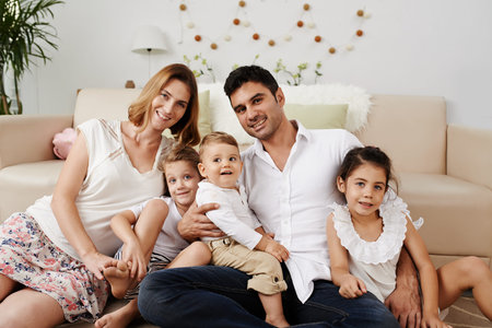 Happy family with three children sitting on the floor in their living roomの写真素材