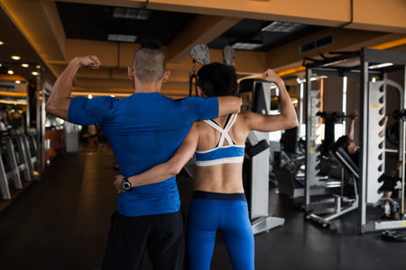 Fit couple hugging and showing their biceps, view from the backの写真素材