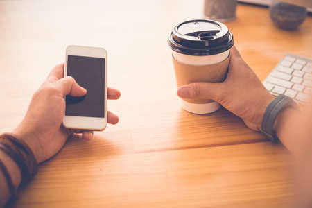 Guy with smartphone drinking take-out coffee and checking out the news feed, first person viewの写真素材