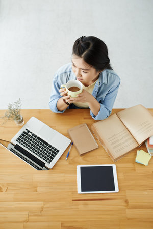 Pensive student at her desk having cup of coffee