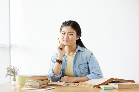 Portrait of smiling Vietnamese student doing homework at her table