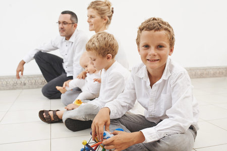 Portrait of smiling boy sitting on the floor with his family in the backgroundの写真素材
