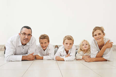 Cheerful family of five lying on the floor and looking at cameraの写真素材