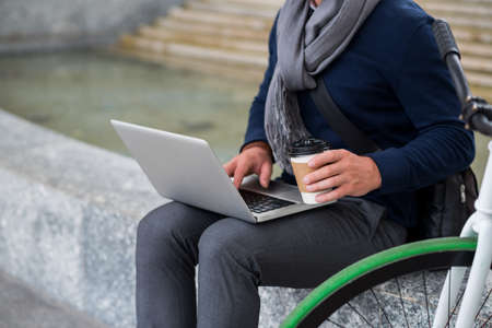 Cropped image of guy drinking coffee and working on laptop outdoorsの写真素材