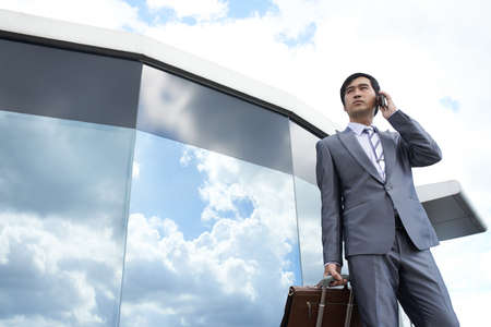 Vietnamese businessman standing outside the airport building and calling on phoneの写真素材