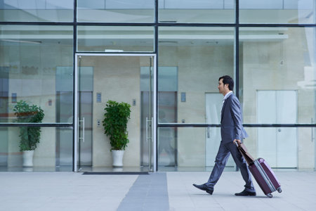 Businessman with suitcase going to terminal of the airport, side viewの写真素材