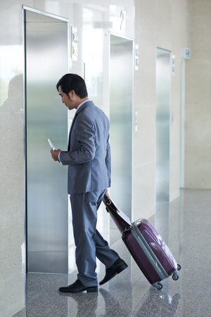 Businessman with suitcase waiting for elevator in airport terminal
