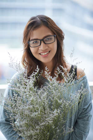 Pretty Indonesian woman in glasses with bouquet of flowersの写真素材