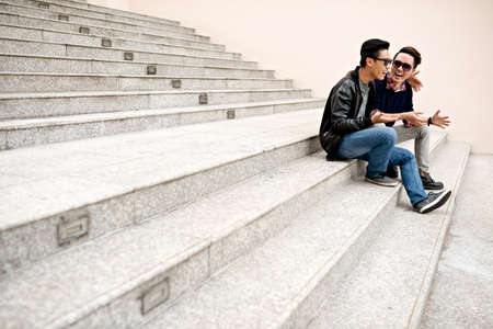 Laughing young male friends sitting on the stairs outdoorsの写真素材