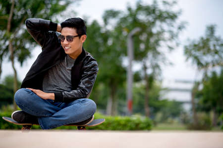 Cool guy in leather jacket and sunglasses sitting on the skateboardの写真素材