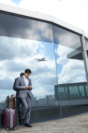 Businessman standing at the building of modern airport and using smartphoneの写真素材