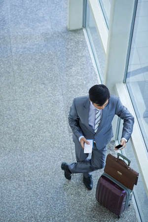 Businessman standing at window in airport terminal and using phoneの写真素材