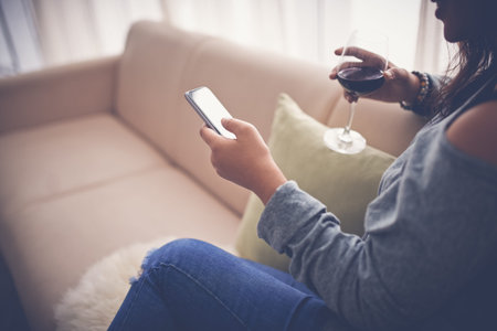 Woman drinking wine and text messaging at homeの写真素材