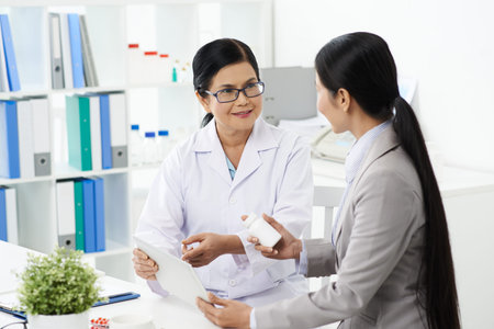 Senior Vietnamese pharmacist explaining effects of drug to business ladyの写真素材